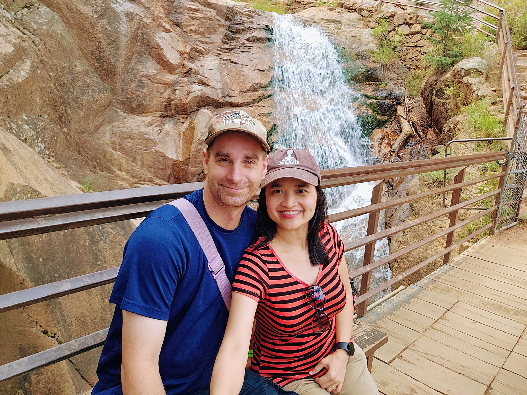 Justin and Jasmin sitting on a wooden platform with a waterfall in the background in Colorado