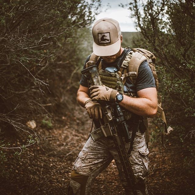 Person in tactical gear holding a rifle in a forest setting