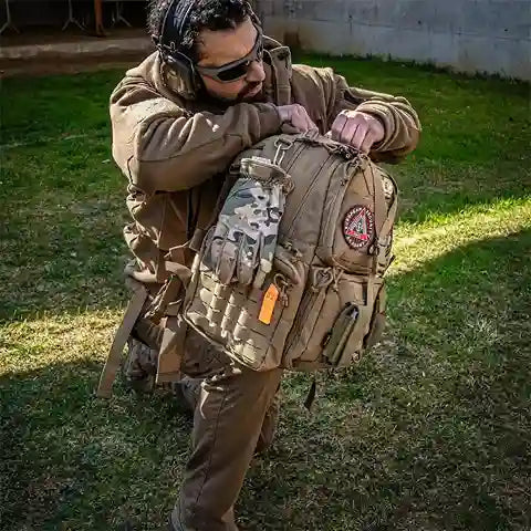 Person in tactical gear hugging a large tactical backpack outdoors.