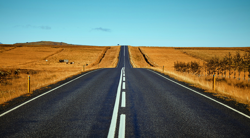 Long straight road stretching into the distance with a clear blue sky.