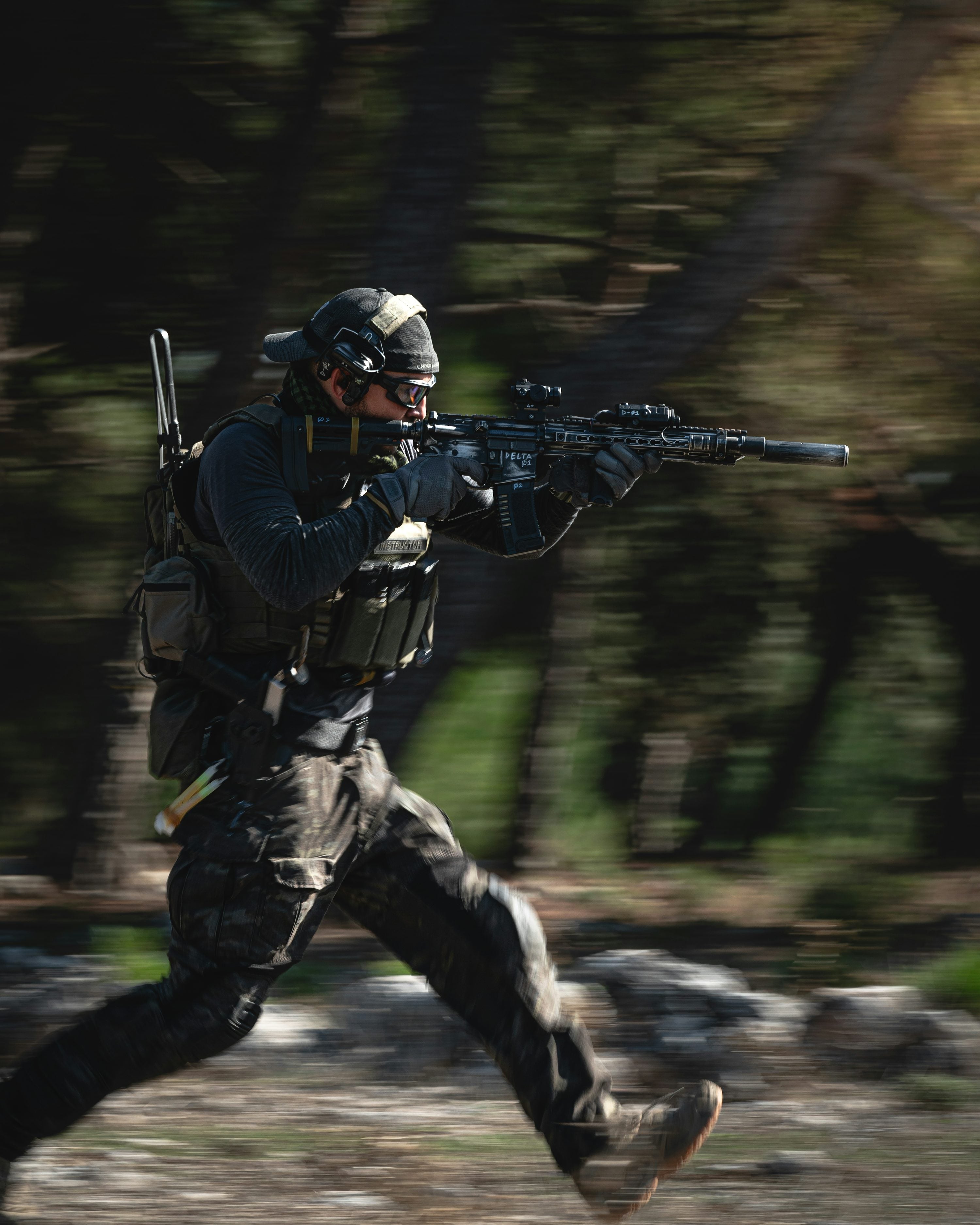 Person in tactical gear running with a rifle through a forest